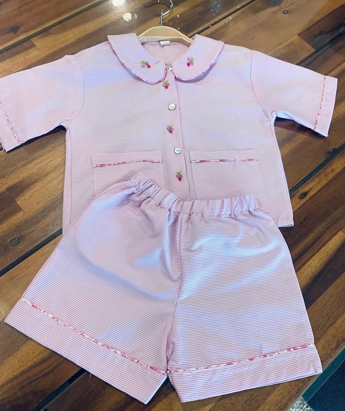 Pink striped pajama set with Peter Pan collar and floral embroidery on a wooden table.