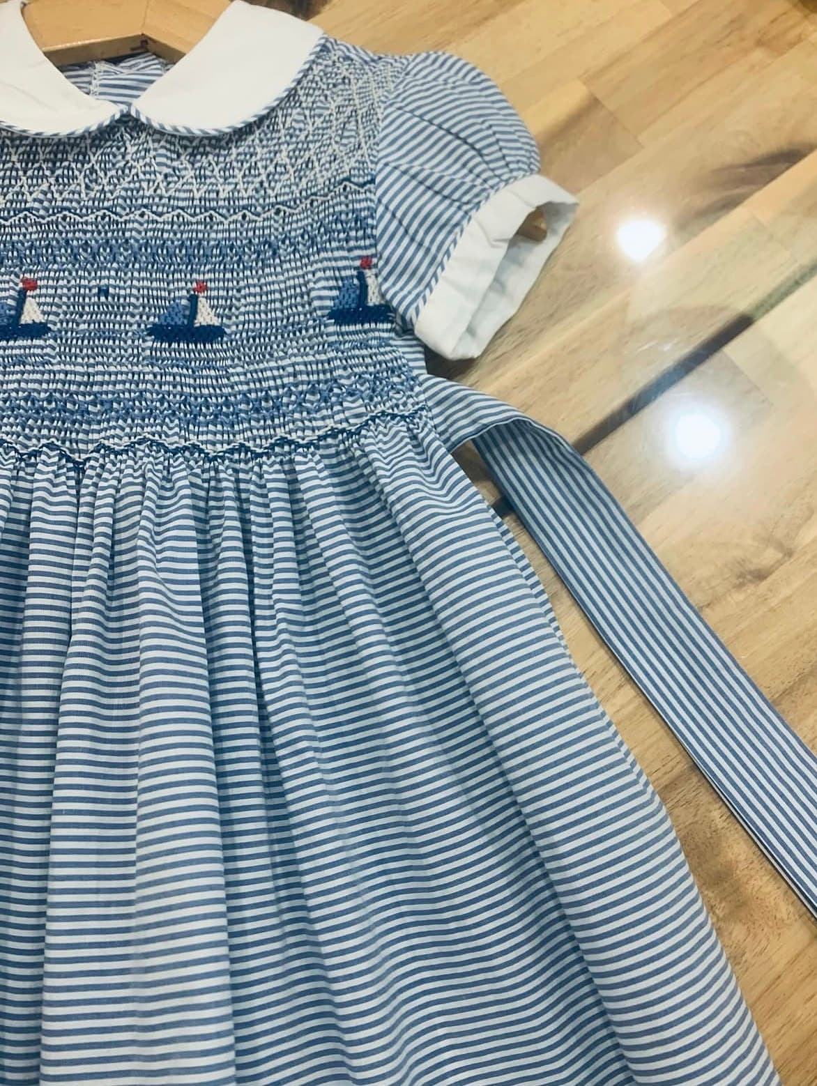 Blue and white striped smocked dress featuring embroidered sailboats and white Peter Pan collar.