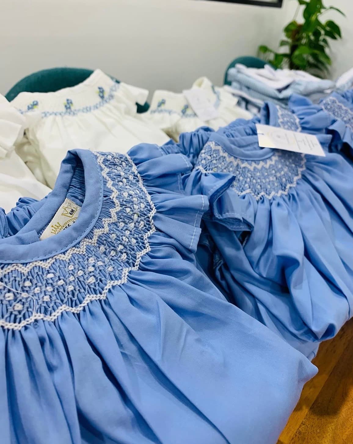 Light blue and white smocked baby dresses with intricate white embroidery and ruffled collars.