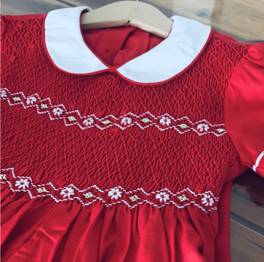 Red smocked children's dress featuring a white Peter Pan collar and embroidered white daisy patterns.